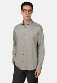 Camicia button-up grigia chiara con maniche lunghe, texture sottile e bottoni neri. Presenta un orlo curvo e un design classico del colletto.