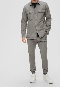 Grijs katoenen shirt met twee borstzakken, gecombineerd met bijpassende taps toelopende broek en witte sneakers. Soepele textuur, met knopen aan de voorkant.