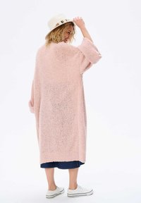 Jasnoróżowy, oversize'owy sweter dzianinowy z rękawami 3/4, teksturowana tkanina i ściągacz u dołu. W zestawie z dżinsową spódnicą i białymi sneakersami.