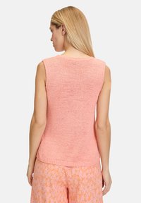 Perzikkleurig mouwloos topje met een ronde halslijn, gebreide textuur en een losse pasvorm, gecombineerd met geprinte oranje broek.