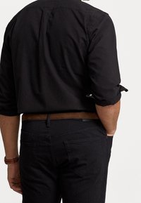 Svart skjorta med knappar och uppvikta ärmar, matchad med mörka jeans och ett brunt läderbälte. Har en subtil textur och fickor på jeansen.