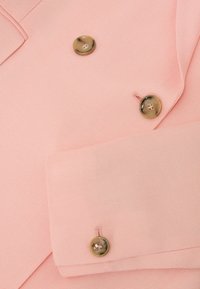 Blazer in tessuto rosa chiaro con trama, con due bottoni dorati con bordo sul davanti e uno sul polsino.