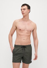 Grønne svømmetights med elastisk liv og snøring, med en sidelomme og en liten logo på nederste venstre ben.