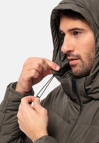 Giacca imbottita marrone con cappuccio. Il modello regola il cordino al collo, dotata di una zip e dettagli elastici. Texture morbida.