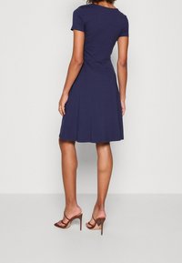 Abito navy blue a maniche corte con gonna svasata, realizzato in materiale morbido. Presenta un collo rotondo e una consistenza liscia, con lunghezza fino al ginocchio.