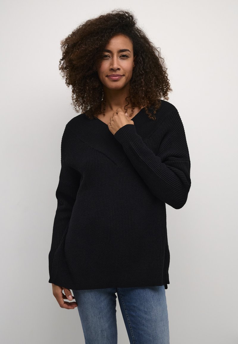 Schwarzer gerippter Pullover mit V-Ausschnitt und langen Ärmeln. Hat eine lockere Passform und Seitenschlitze und wird mit Jeans kombiniert.