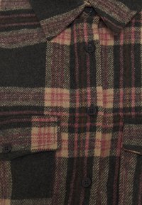 Plaid shirt made of wool in dark green, beige, and burgundy. Features a collared neck, buttoned front, and two chest pockets.