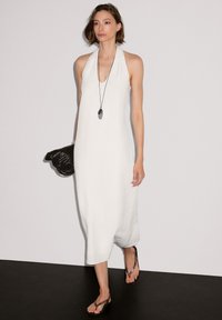Weißes Neckholder-Kleid mit lässiger Passform, knielang, kombiniert mit einer schwarzen geflochtenen Tasche und Flip-Flops. Glatte Textur und minimalistisches Design.