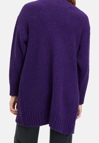Lila oversized cardigan med ett texturerat stickat mönster, ribbade kanter och en lång, svävande baksida. Enkel design med droppade axlar.