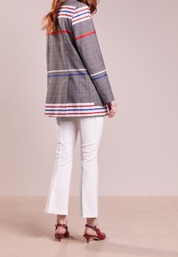 Blazer grigio a scacchi con strisce rosse, blu e bianche, abbinato a pantaloni flared bianchi e sandali con tacco rossi. Tessuto liscio, vestibilità su misura.