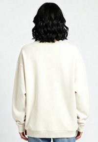 Felpa oversized crema realizzata in morbido tessuto, con spalle scese e polsini a costine, mostrata da dietro.