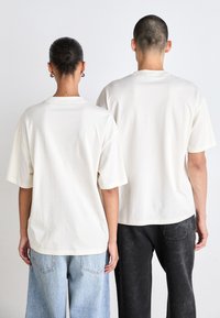 Kortærmede, krèmefarvede t-shirts med en afslappet pasform, vist på to personer, med blød bomuldsstruktur og minimal syning.