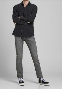 Camisa negra de manga larga con dos bolsillos en el pecho, combinada con jeans gris claro y zapatillas altas negras con suelas blancas.