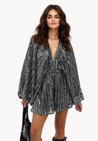 Robe en sequins noirs et argentés avec un décolleté en V profond, des manches ballons longues et une taille cintrée, présentant des rayures verticales et une jupe joyeuse.