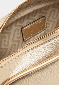 Gouden leren tas interieur met een gladde rits en een merklabel, voorzien van een gemusterde voering in een neutrale kleur.