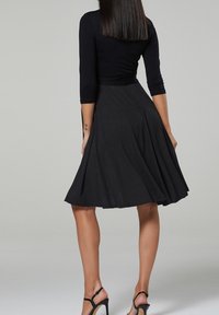 Vestido negro con mangas tres cuartos y falda de lunares. Diseño acampanado con una textura suave, combinado con tacones negros de tiras.