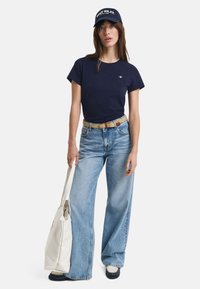 Navy cotton t-shirt, high-waisted light blue wide-leg jeans, patterned belt, white canvas tote bag, black shoes, and navy cap with text.