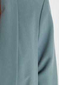 Zbliżenie jasnoniebieskiego materiału z widocznym szwem i subtelną teksturą skosu.