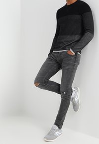 Maglione a blocchi di colore nero e grigio con design testurizzato, abbinato a jeans grigi slim fit consumati e sneakers grigio chiaro.