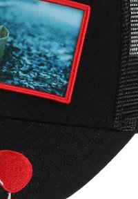 Schwarze Mütze mit einem gebogenen Schirm, die auf der Vorderseite mit einem rechteckigen Fotopatch, umrandet in Rot, und einer roten Luftballon-Stickerei versehen ist.