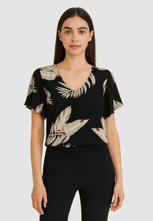 Blusa nera a maniche corte con scollo a V, decorata con motivi di foglie beige e ruggine, realizzata in un tessuto leggero. Abbinata a pantaloni neri.