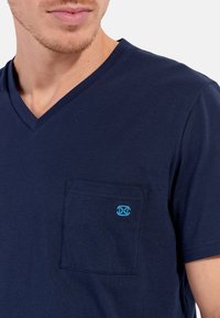 Navyblaues V-Ausschnitt-T-Shirt aus weichem Baumwollmaterial, mit einer kleinen Brusttasche auf der linken Seite, die ein kleines blaues Logo zeigt. Einfaches Design, kurze Ärmel und lockere Passform.