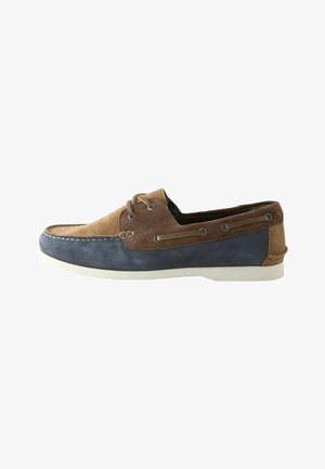 Męskie casualowe buty boat w brązowym i granatowym zamszu z białą podeszwą i sznurowanym detalem wokół kołnierza pięty.