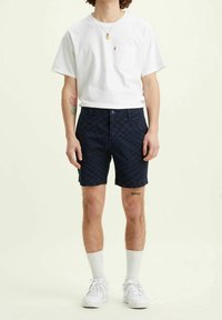 Tummansininen ruudullinen shortsit, jotka on valmistettu pehmeästä kankaasta. Shortsien varusteina on vetoketjuluukku, etutaskut, ja ne on yhdistetty valkoiseen t-paitaan ja valkoisiin tennareihin.