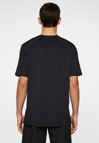 Svart t-shirt med kort ärm och en mjuk textur, med rundad halsringning och subtila sömdetaljer. Baksidan är enkel utan grafik.