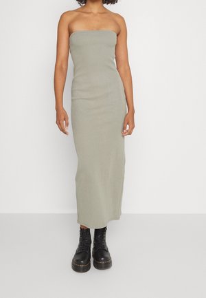 Olijfgroene strapless maxi-jurk van geribbelde stof, met aangesloten silhouet en enkellengte ontwerp. Gecombineerd met zwarte veterlaarzen.