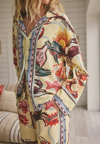 Set de pijama cu model din material galben, având ilustrații cu viața marină, bărci și text. Marginile sunt decorate cu accente albastre și roz.