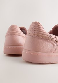 Baskets en cuir rose avec une finition texturée, dotées de coutures en relief et d'une semelle en caoutchouc lisse. Design arrondi avec des accents minimalistes.