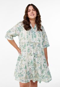 Robe florale légère avec un design en niveaux, arborant des imprimés botaniques verts et jaunes, des manches courtes et une patte de boutonnage.