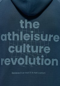Felpa blu scuro con una trama morbida. Presenta una grande scritta grigia chiara che dice "la rivoluzione della cultura athleisure" e un sottotitolo più piccolo sotto.