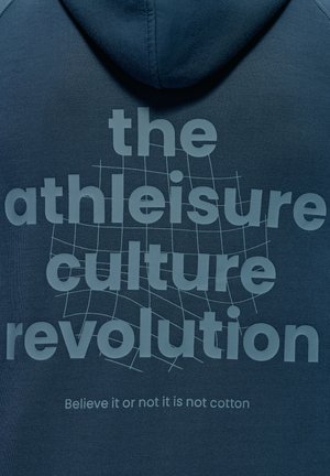 Tmavomodrá mikina s mäkkou textúrou. Na prednej strane sa nachádzajú veľké svetlošedé písmená s nápisom "revolúcia kultúry athleisure" a pod ním menší slogan.
