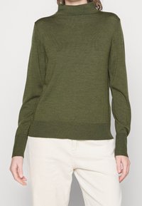 Olive green knitted sweater with a high neckline, long sleeves, and ribbed cuffs and hem. The texture is smooth with a light weight.