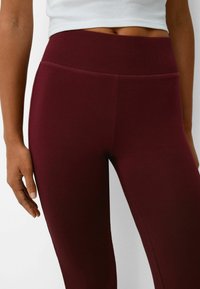 Leggings bordeaux en matériau extensible, dotés d'une large ceinture lisse et d'un design ajusté qui épouse les jambes.