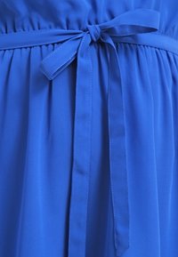 Robe en tissu bleu avec une ceinture nouée à la taille et des plis froncés en dessous de la ceinture.