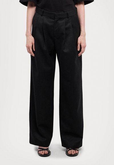 Sorte vide benbukser med læg, skræddersyet design, tekstureret stof og glat talje. Båret med flade sandaler.