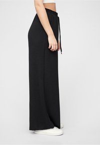 Black, long, wide-leg pants with a gathered, elastic waistband and drawstring. Made of soft material, featuring a smooth texture.