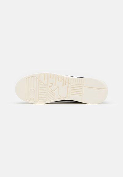 Balts sneakeru apakšējais slānis, kas izgatavots no teksturēta gumijas, nodrošina saķeri, ar tīru dizainu un diskrētām rakstainām rievām, kas nodrošina noturību un vilkmi.