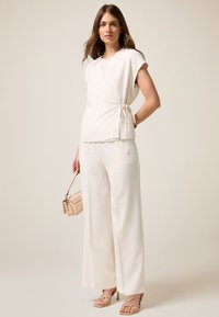 Top ivory cu mâne scurte, cu detaliu legat la talie, asortat cu pantaloni largi ivory și sandale bej cu barete.