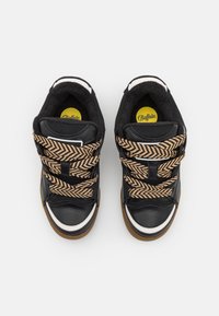 Zwarte sneakers met een chunky ontwerp, witte accenten en veters met een visgraatmotief. Het interieur heeft een gele logo op een ronde inlegzool.