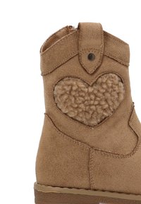 Botín de tobillo de ante marrón con un detalle en forma de corazón en tejido beige suave, que incluye una correa en el tobillo y una suela de goma texturizada.