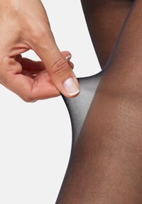 Medias negras transparentes estiradas con los dedos, mostrando una textura suave y ligera y un tejido fino y uniforme en todo su recorrido.
