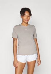 Camiseta atlética de color gris claro, de manga corta, con escote redondo, hecha de material transpirable; presenta un detalle de logo en la parte frontal.