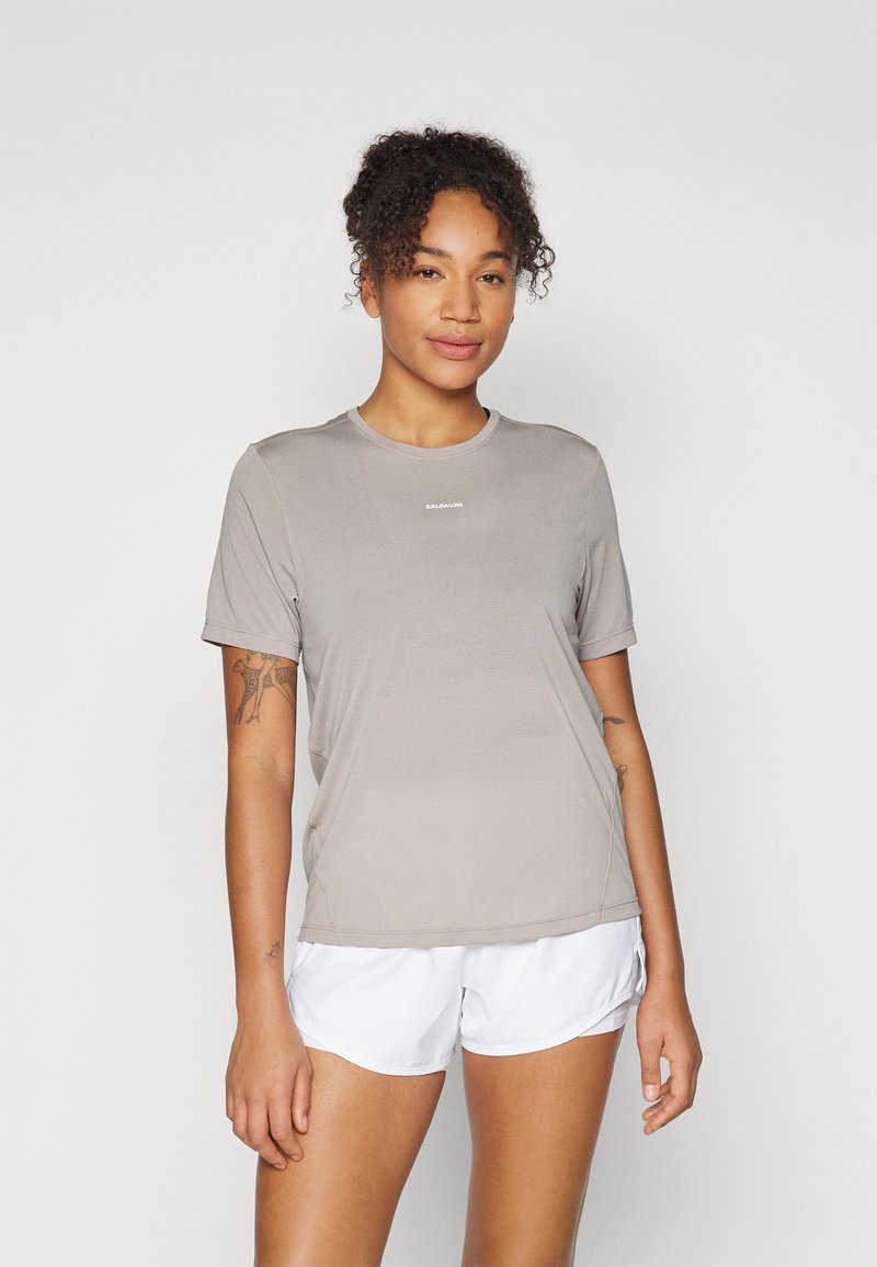 Camiseta atlética de color gris claro, de manga corta, con escote redondo, hecha de material transpirable; presenta un detalle de logo en la parte frontal.