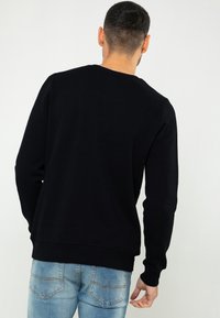 Zwarte sweatshirt met lange mouwen, ronde halslijn en geribbelde manchet, gecombineerd met lichtblauwe jeans, getoond van achteren.