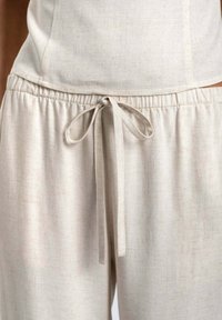 Pantalones de lino de color claro con cinturilla elástica y cordón. Textura suave con sutiles variaciones en la tela.