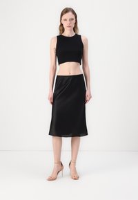 Svart cropped topp med erm løs design kombinert med en flytende svart sateng midi skjørt. Gjennomsiktige stiletto sandaler fullfører stilen.
